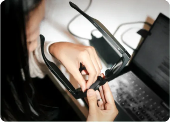Hands assembling a smart glasses prototype beside a laptop